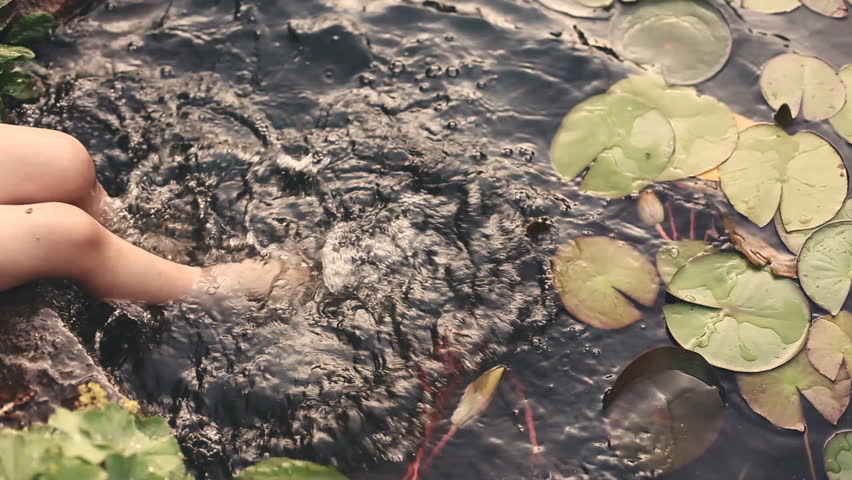 Baby feet playing in the water of pond with lilies