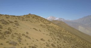 Forward advancing, elevating aerial drone view hugging hillside panning left to reveal deep Lupra valley and 7th tallest Dhaulagiri Himalaya mountains landscape in Muktinath, Nepal. 4k 1.9:1 23.976fps
