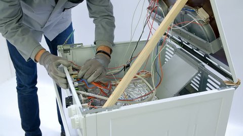 A young man is unplugging wires of different colours in the stove. He is using safety gloves.