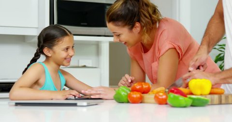 Girl using digital tablet with mother while father cutting vegetables in kitchen at home Social distancing and self isolation in quarantine lockdown for Coronavirus Covid19