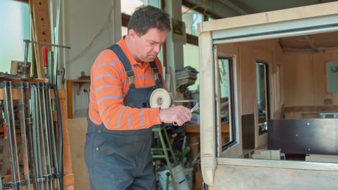 A middle-aged woodworker is using two types of wrenches to adjust the car mirror on a vintage car that he is designing in his workshop at home.