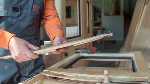 A man is putting a wooden panel through a handle. He is making a vintage car in his workshop at home.