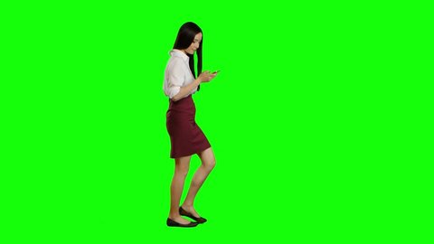 Girl walks and holds a phone and looks at photos. Green screen. Side view