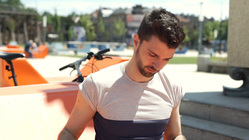Handsome man plays music on smartphone and listening it in the city, steadycam shot
