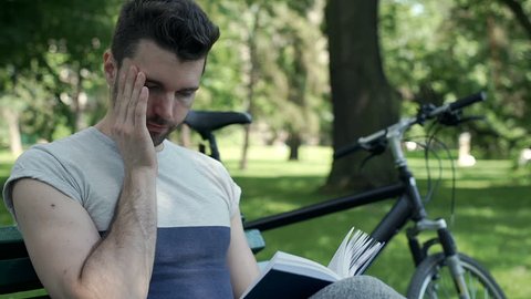 Handsome man stops reading book because of painful headache, steadycam shot
