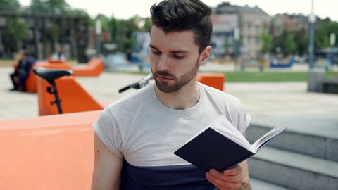 Handsome man answers cellphone while reading book in the city, steadycam shot
