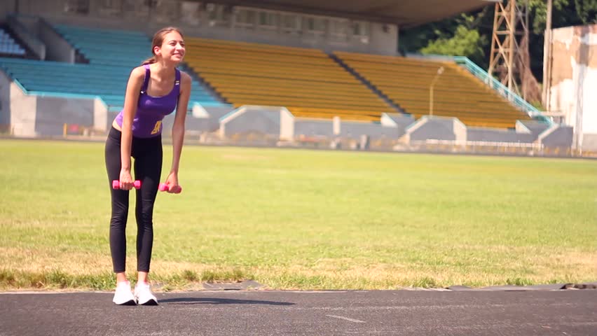Young girl doing exercises with barbell in the stadium
