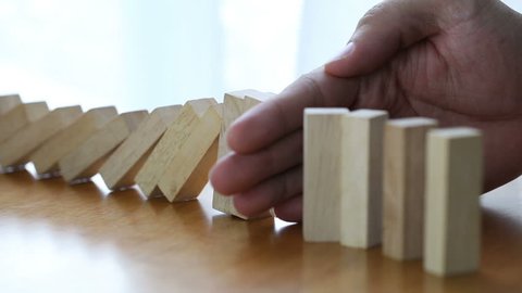 Male hand stopping the domino effect. Risk control concept 