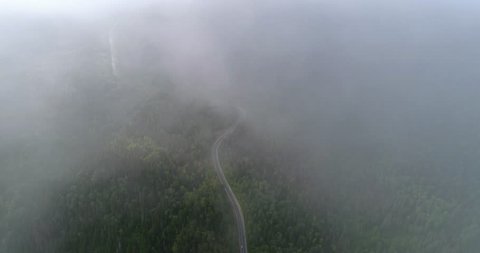 Flight in the clouds. A view of the earth through the clouds. A winding mountain road. The road is on the heights of the forest hills. Aerial View.