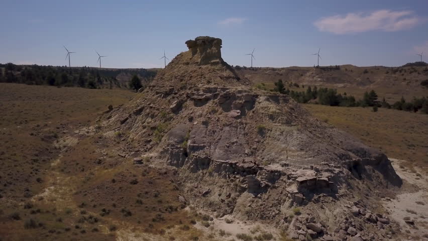 flying counter clockwise around small butte in Montana with wind farm on horizon
