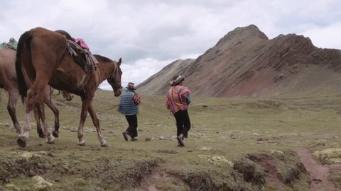 Peruvian men wearing a highlander hats walking with horses on the mountains of Peru. Slow motion