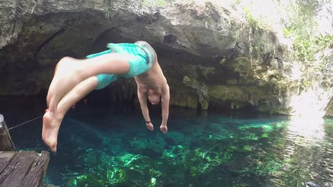 SLOW MOTION CLOSEUP Young men on vacation in sunny Mexico diving into crystal clear cenote water. Cheerful male in blue boardshorts jumping head first into fresh water in Mexican Grand Cenote sinkhole