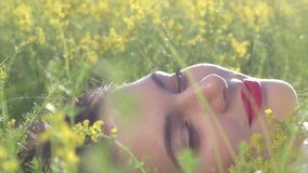 Beauty young woman lying on blooming field and smelling wild flowers. Beautiful happy girl enjoying nature outdoor. Pollen Allergy free concept. Slow motion 240 fps 4K UHD video 3840x2160