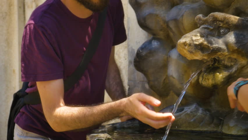 Young Man Drinking Water from ancient Fountain in villa borghese Park Rome