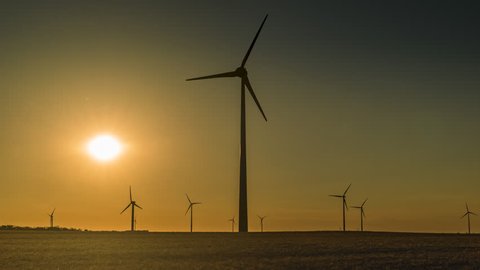 Timelapse of working wind turbines in wheat fields during colorful summer sunset