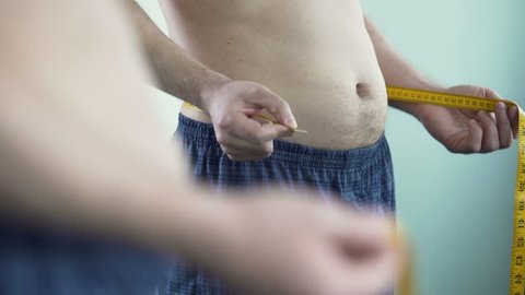 Male with middle-aged crisis measuring his body size, afraid of getting fat