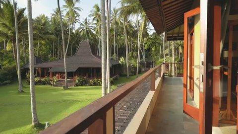 Open doors on long balcony, view of wooden jogjo house and palm trees, Bali
