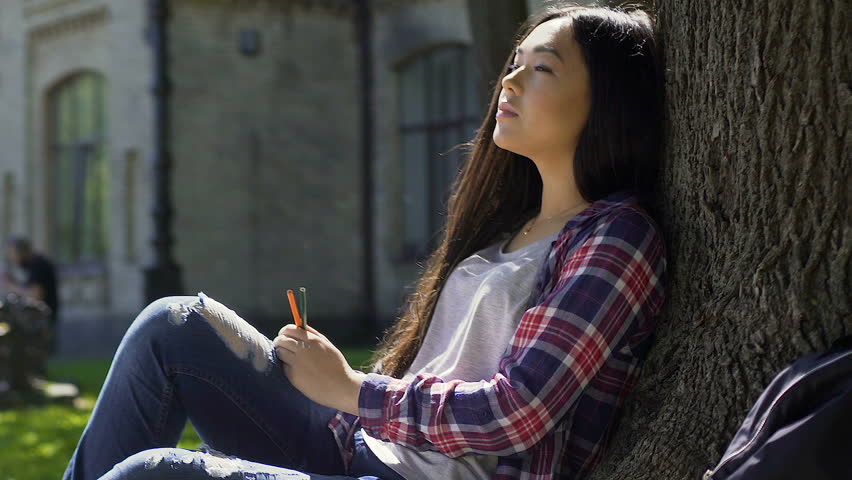 Mixed-race girl looking for inspiration sitting under tree in warm rays of sun