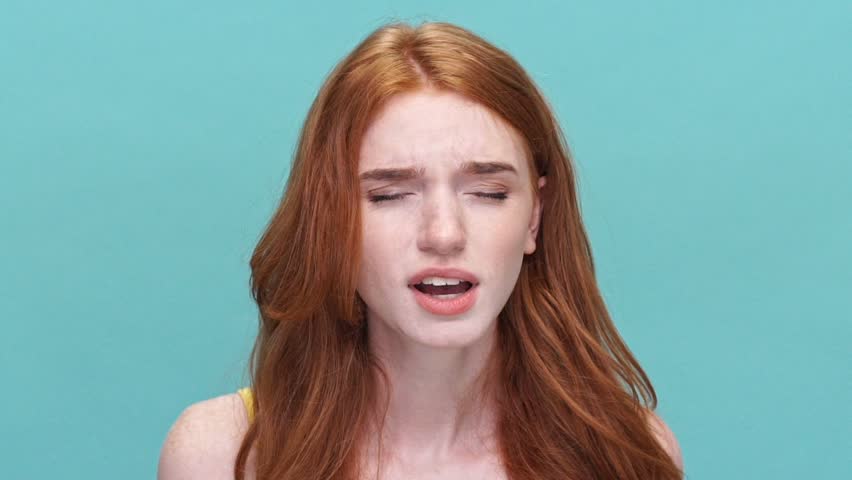 Close up of a young stressed redheaded girl shouting isolated over blue background | Shutterstock HD Video #28892719