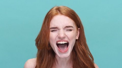 Close up of a young stressed redheaded girl shouting isolated over blue background
