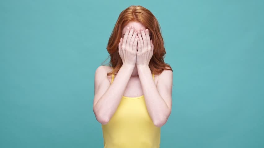 Smiling redheaded girl playing hide and seek while covering her eyes with palms isolated over blue background Royalty-Free Stock Footage #28892737