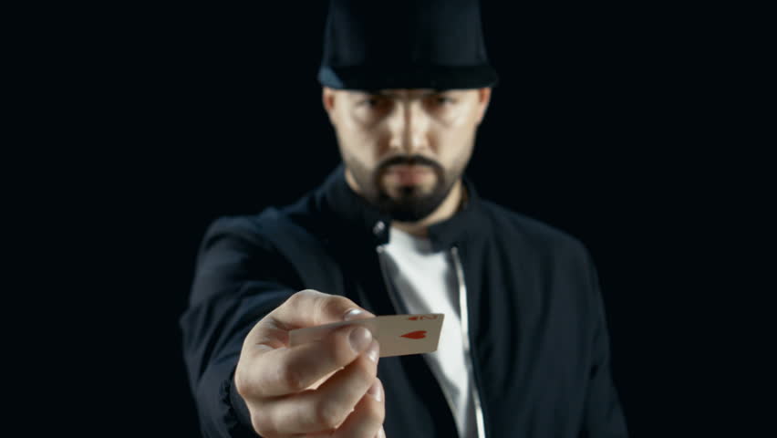 Professional Street Magician in a Cap Performing Sleight of Hand Card Tricks, Spinning One Card on a Finger. Background is Black. Shot on RED EPIC-W 8K Helium Cinema Camera.