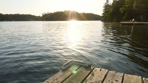 Slow motion shot of freshwater lake and sunshine with dock and cottages. Cottage country in Ontario, Canada.
