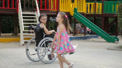 A girl with a broken leg sits in a wheelchair in front of the playground