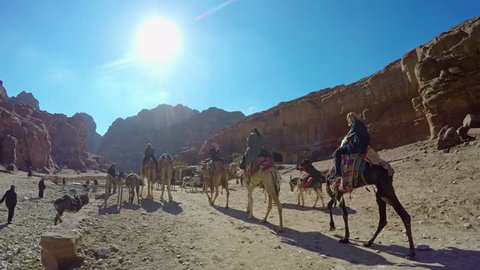 PETRA, JORDAN - circa JAN, 2017:  Tourists ride on camels near Royal Tombs in Petra, originally known to Nabateans as Raqmu - archaeological city in Jordan. Silk and Urn Tombs on background