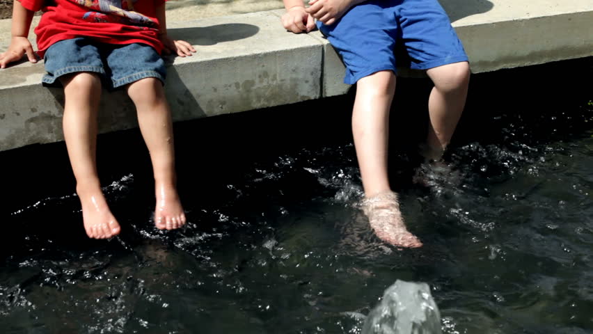 Friends with water sitting in fountain kicking feet.