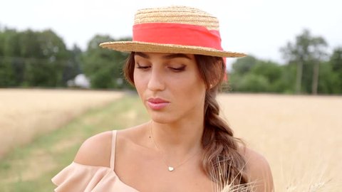 Woman with long hair and hat walks on path near wheat field during summer afternoon
