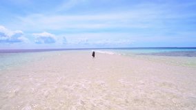4k Aerial drone quadcopter footage of young woman walking on beach with beach bag and sun hat on white sand island in blue water tropical ocean bay on holiday. 