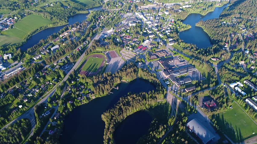 4K aerial view of small town with sport field, houses, lakes, and forest. Camera moving forward looking down and forward. Summer evening at city of Suonenjoki, Finland. Scandinavia.