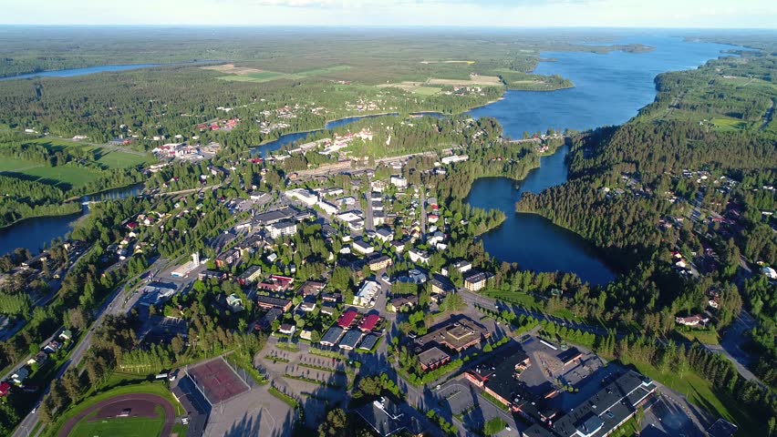 4K aerial view of small town with sport field, houses, lakes, and forest. Camera looking at horizon and slowly moving looking down. Summer evening at city of Suonenjoki, Finland. Scandinavia.