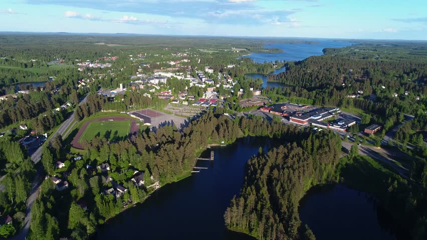 4K aerial view of small town with sport field, houses, lakes, and forest. Camera moving from looking towards horizon. Summer evening at city of Suonenjoki, Finland. Scandinavia.