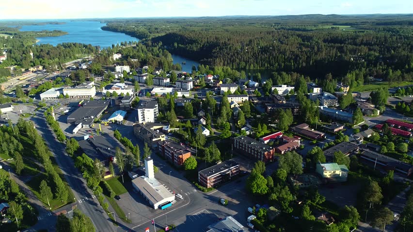 4K aerial view of small town with streets, houses, lakes, and forest. Camera moving forward looking towards horizon and rotating slowly. Summer evening at city of Suonenjoki, Finland. Scandinavia.