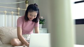 Clip movement of Asian Young girl sitting and using laptop computer to play or working on the mattress in bedroom, lifestyle concept
