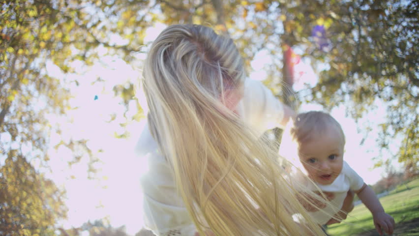 Portrait of attractive young blonde European mum bouncing her young baby boy in her arms outdoors RED EPIC