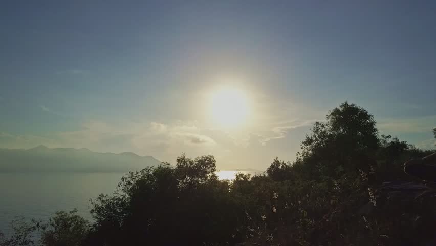 backside view young athletic girl silhouette sits in Padmasana on rock against plants and large bright sun