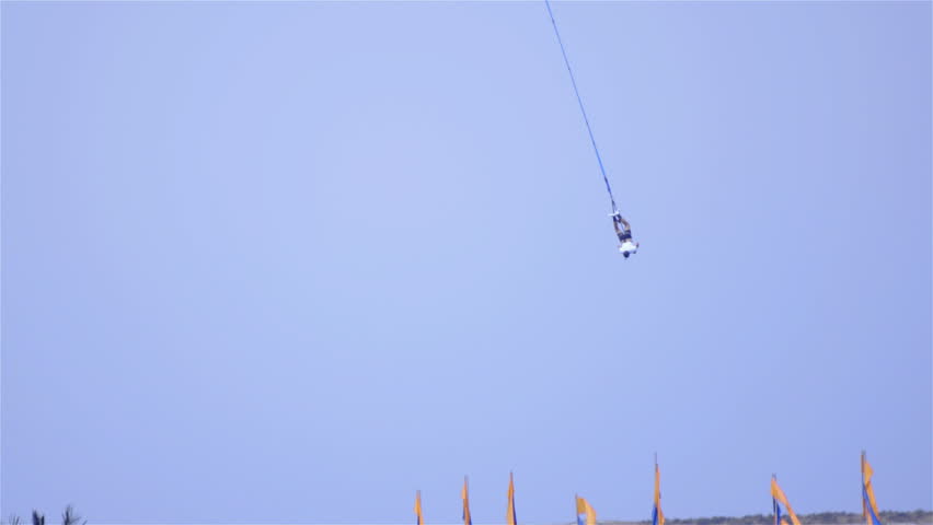 Person swing around on bungee rope 4K. Long shot of unknown person hang down after a bungee jump. Blue sky in background.