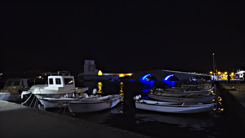 Harbour with fishing boats at night 4K. Static shot of boats in focus wave on sea at night. Single light shining on few boats. Surrounded with darkness.