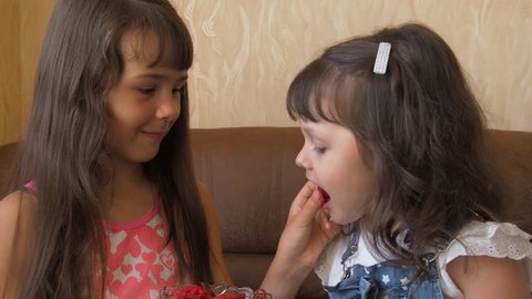 Little girls eat raspberries. Two sisters feed each other raspberries.