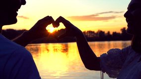 Sun in hands. Beauty Girl and her Handsome Boyfriend making shape of Heart by their Hands against beautiful sea sunset on horizon. Love. Nature. Vacation. Hope. Freedom. 4K UHD video 3840x2160