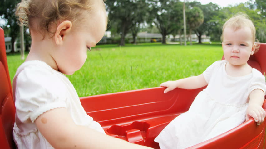 Cute Caucasian girls twins playing together in plastic cart outdoors in the park RED EPIC