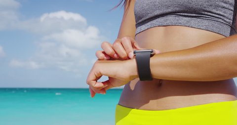 Fitness woman runner woman wearing smartwatch touching and swiping screen. Closeup of smart watch and fit woman on beach using smart watch app. RED EPIC SLOW MOTION.