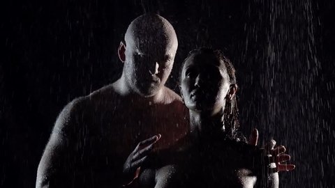 silhouettes of couples at night in the rain. a large bald man holding his woman by the shoulders. unfolds her to him and kisses her on the lips