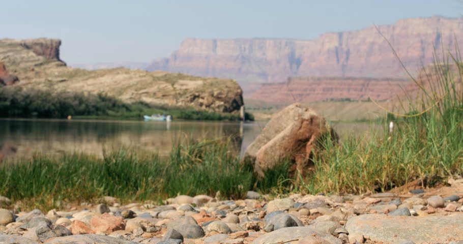 rack focus desert rocky path with grass to rafts boats on the Colorado river with red rock mountain formations in the background in the Grand Canyon National Park, Arizona 4K 
