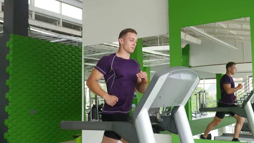Young man running on treadmill and drinking water.
