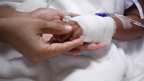 Close up of young parent and sick little daughter holding bandaged hands for comfort in a hospital bed