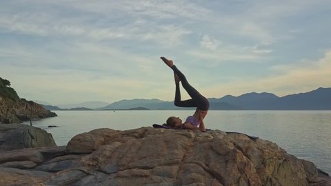 drone view girl bends knee lying in yoga pose Sarvangasana against pictorial green hilly coast at sunrise
